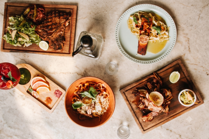 Assorted meals on wooden and ceramic platters, featuring steak, pasta, and seafood, arranged on a marble surface.
