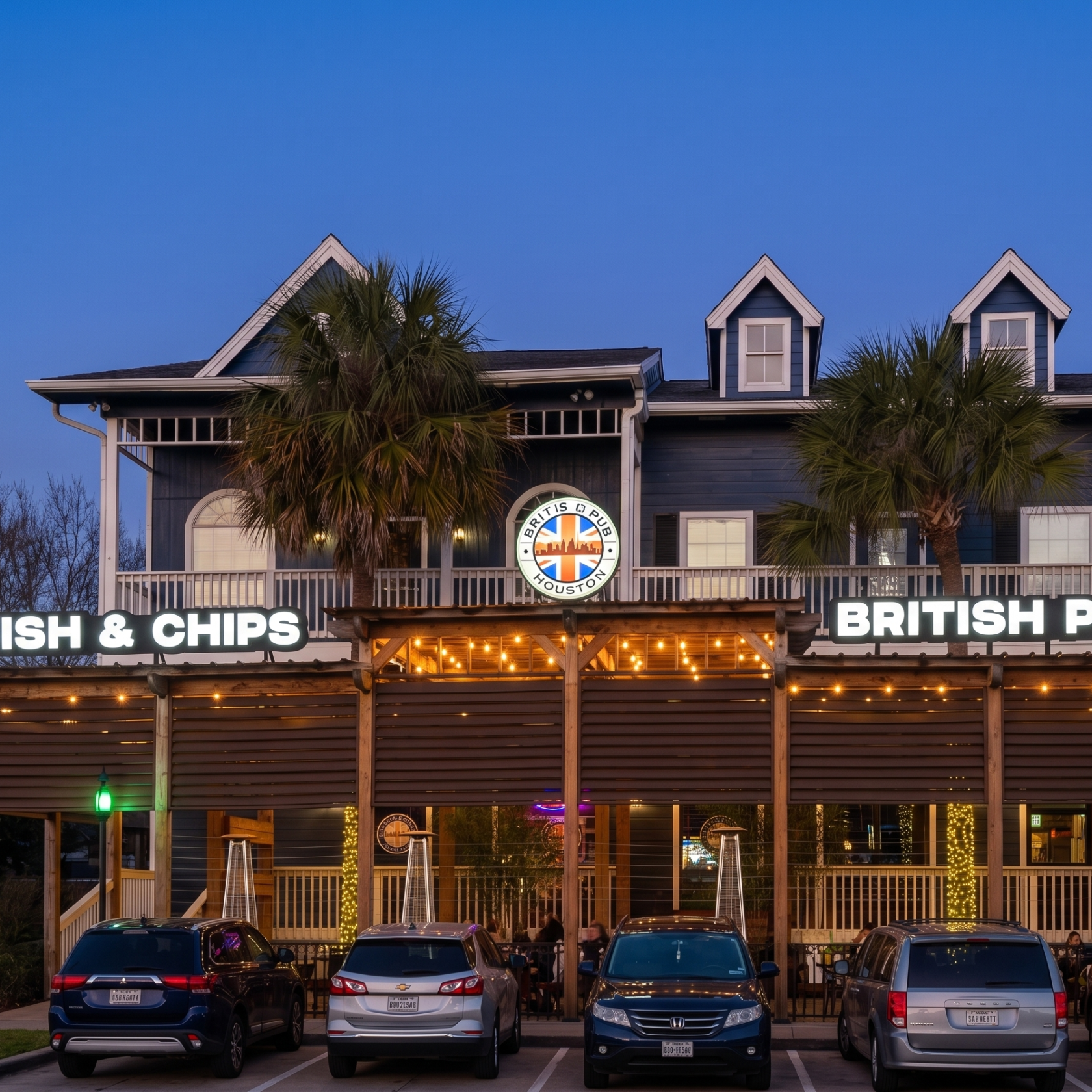Exterior of a British pub with 'Fish & Chips' sign and parked cars at dusk.