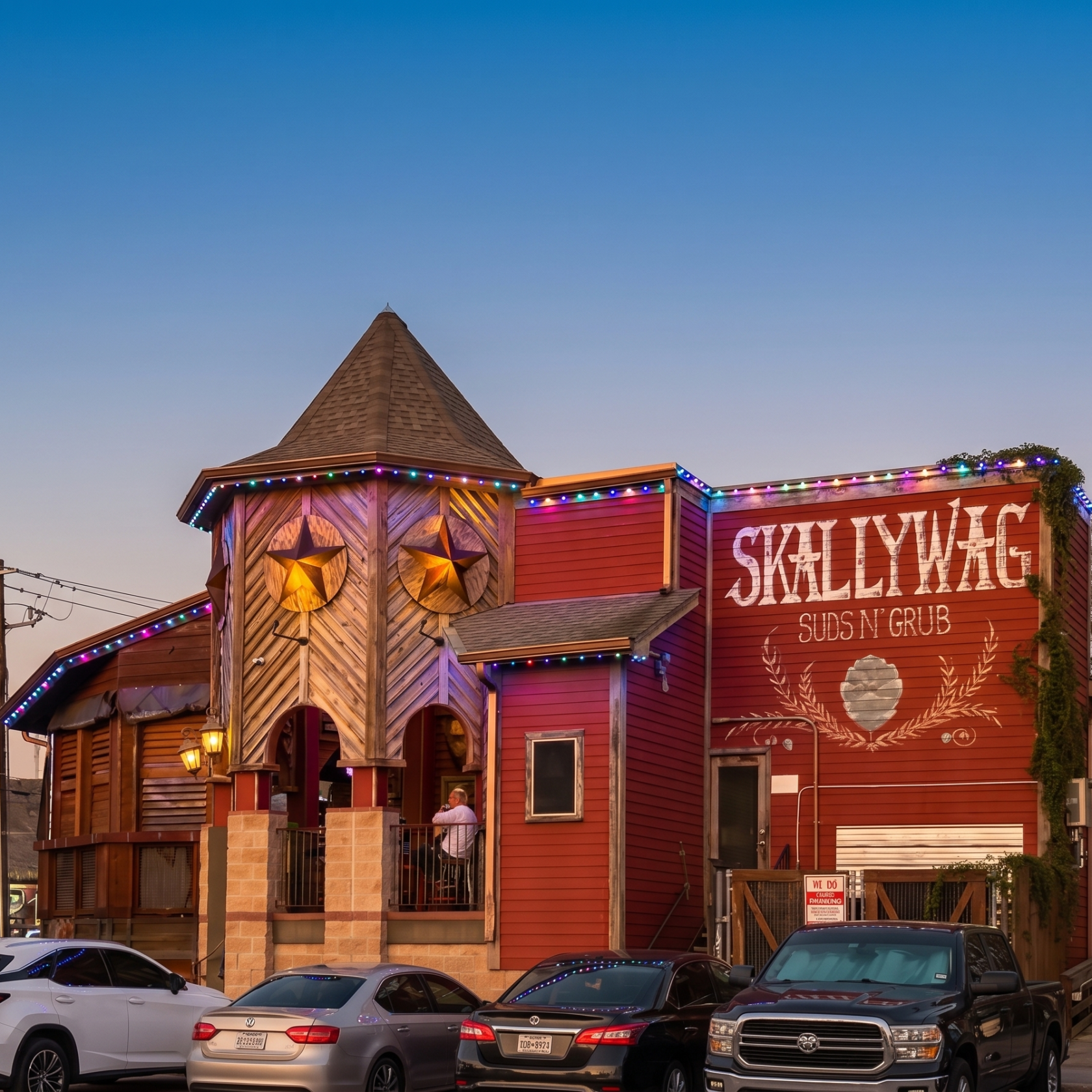 Red building with tower, cars parked in front, sign says 'SKALLYWAG Suds N' Grub'.