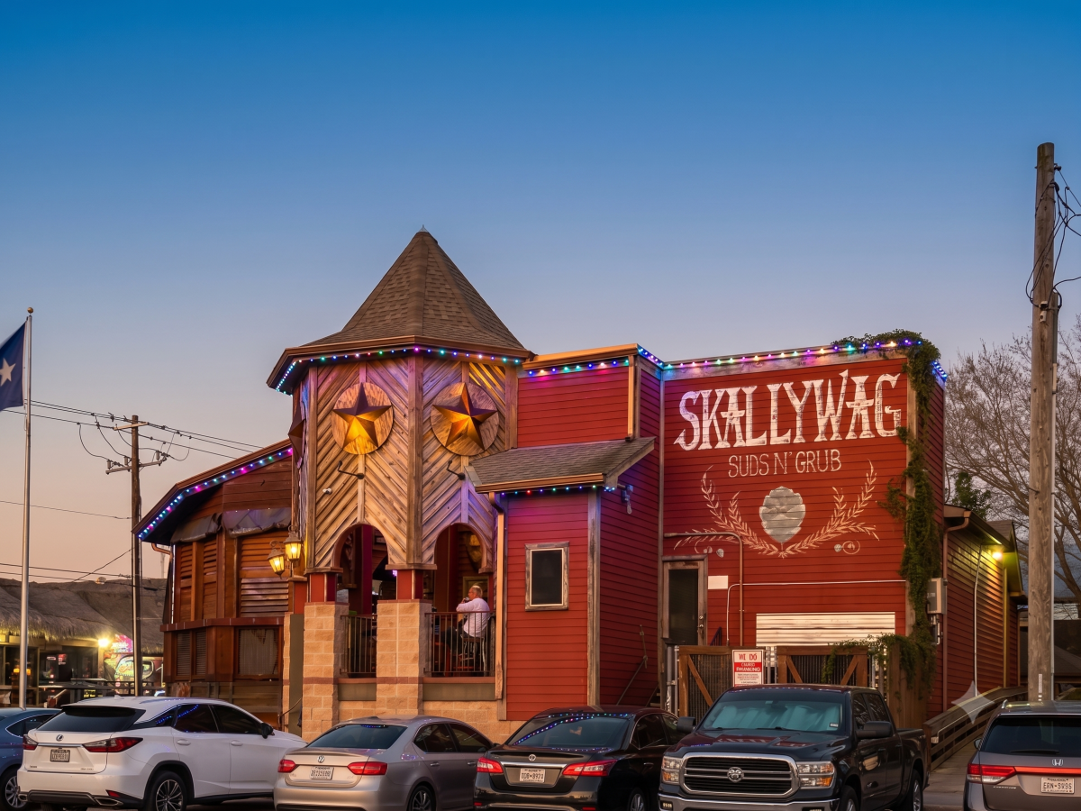 Red building with tower, cars parked in front, sign says 'SKALLYWAG Suds N' Grub'.