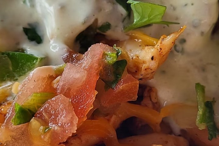 Close-up of a taco with chicken, cheese, tomatoes, and sauce.