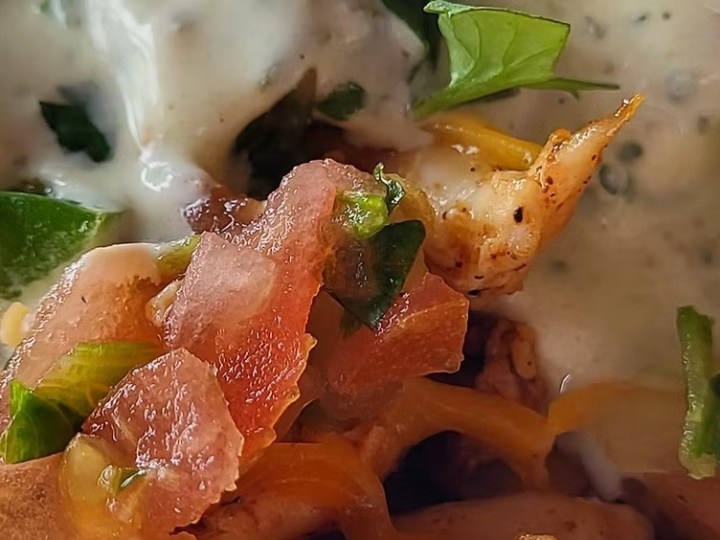 Close-up of a taco with chicken, cheese, tomatoes, and sauce.