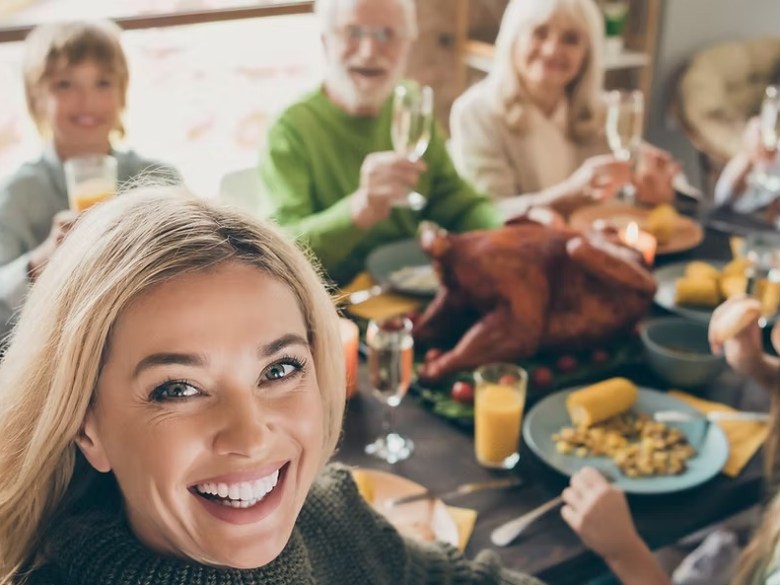 Smiling family of eight at a dinner table with a roast turkey and drinks.