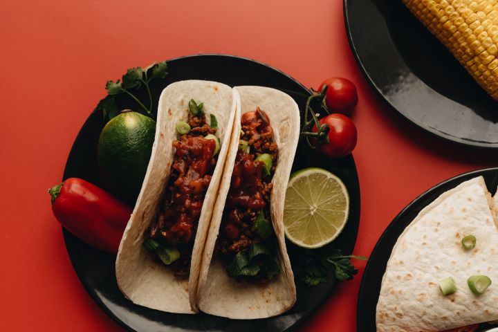 Tacos with lime, cherry tomatoes, and corn on plates.