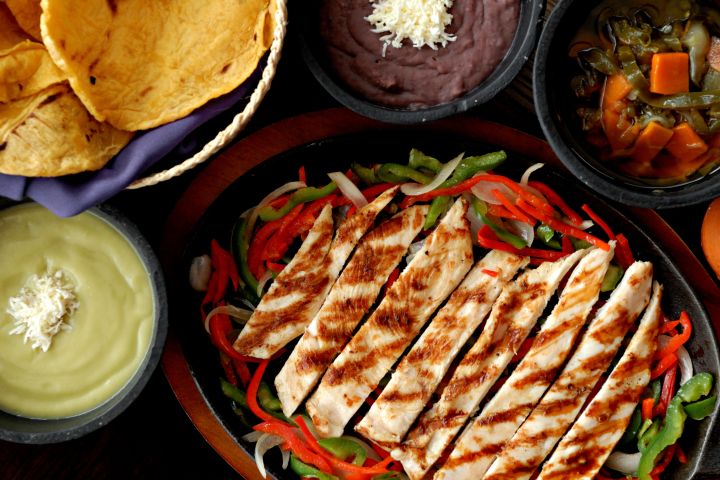 Grilled chicken with vegetables, tortillas, and dips in small bowls.