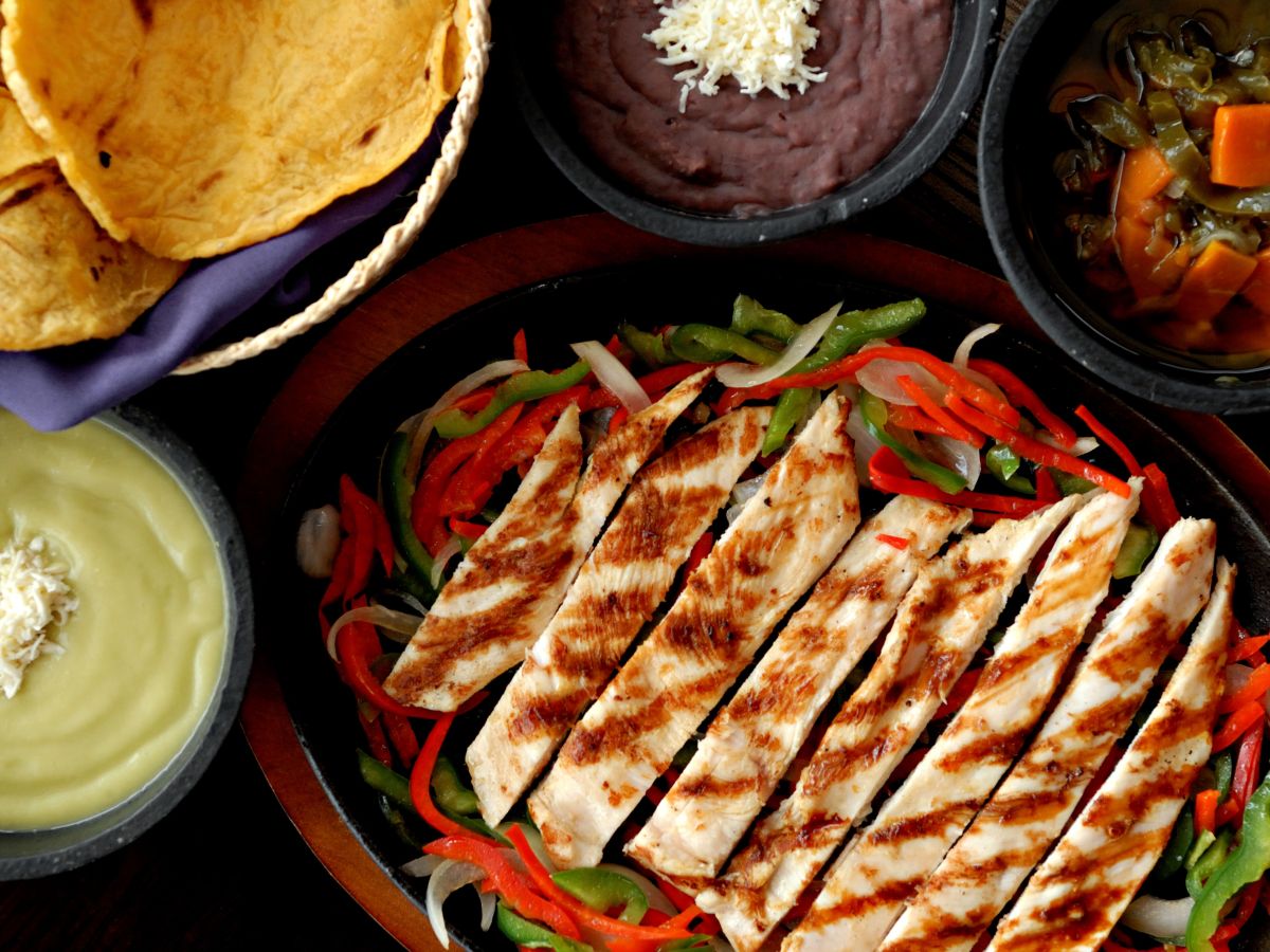 Grilled chicken with vegetables, tortillas, and dips in small bowls.