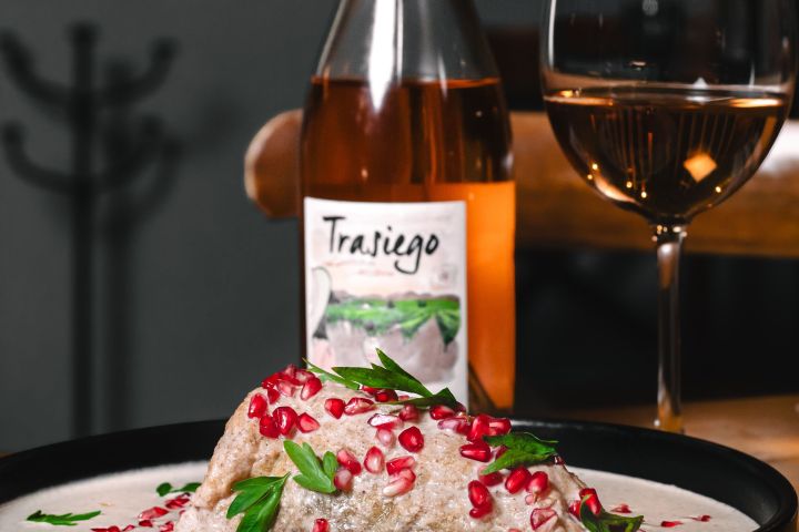 Chiles en nogada dish with pomegranate seeds, beside a wine bottle and glass on a wooden table.
