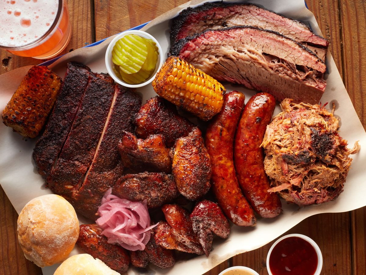 Platter with assorted BBQ meats, corn, pickles, and beer.