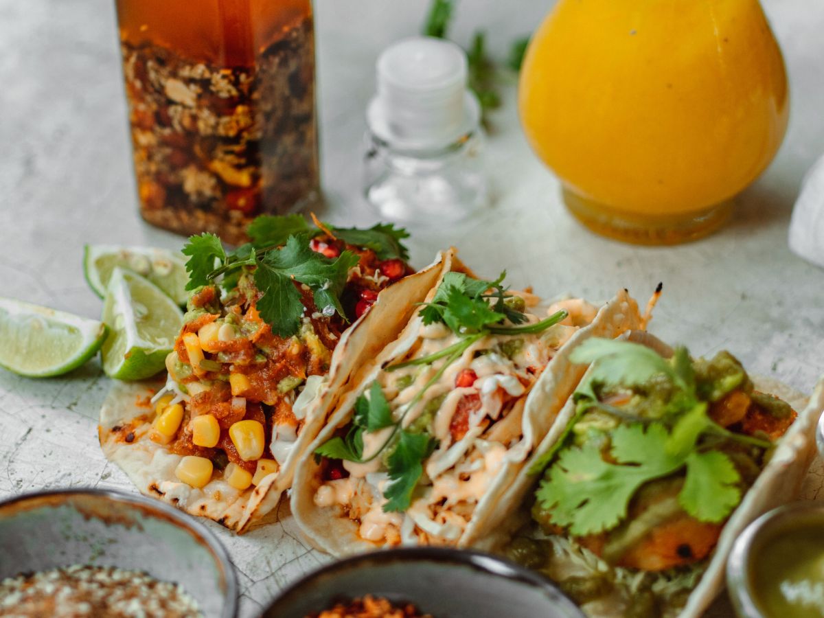 Tacos with toppings, sauces, and drinks on a gray surface.