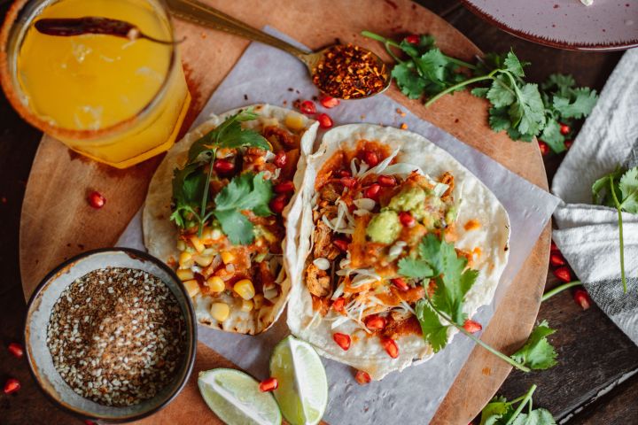 Two tacos with toppings on a round board, garnished with lime and cilantro.